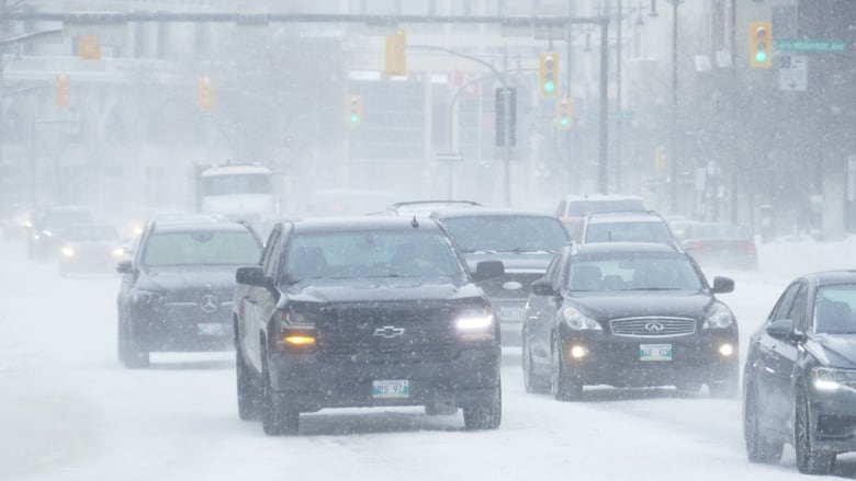 Vehicles drive through downtown Winnipeg during a blizzard.