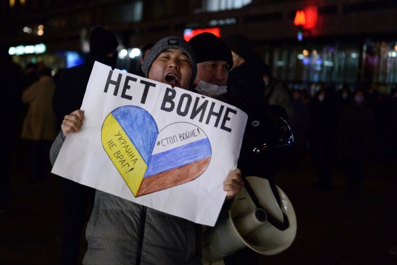 A man with his mouth wide open is holding a sign in front of himself and a megaphone. 