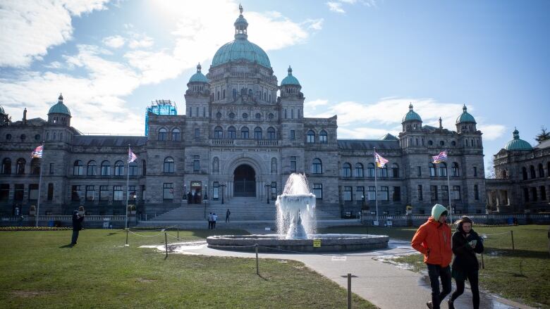 The B.C. Legislature building during winter, with two people walking past the fountain at the entrance.