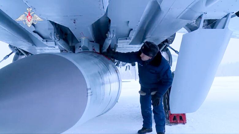 A technician inspects a missile underneath a fighter jet.