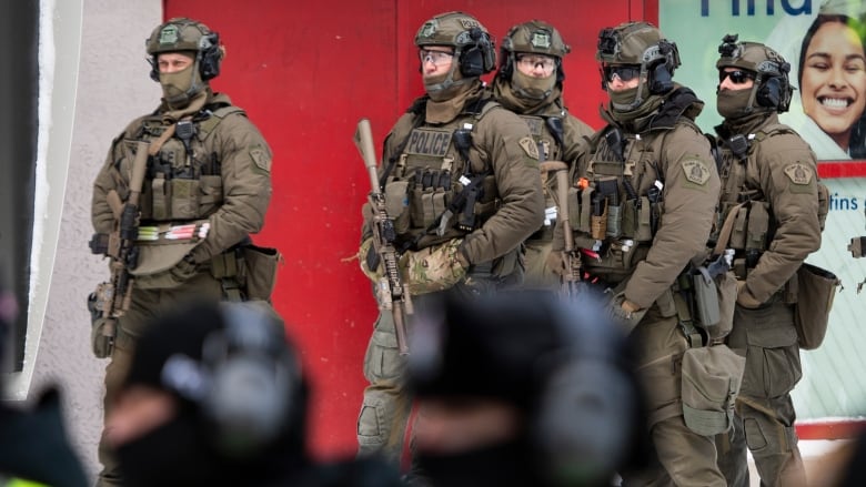 RCMP tactical officers stand behind uniformed officers as they prepare to clear protesters from a blockade of vehicles on Rideau Street, as police aim to end an ongoing protest against COVID-19 measures that has grown into a broader anti-government protest, on its 22nd day, in Ottawa, on Friday, Feb. 18, 2022.