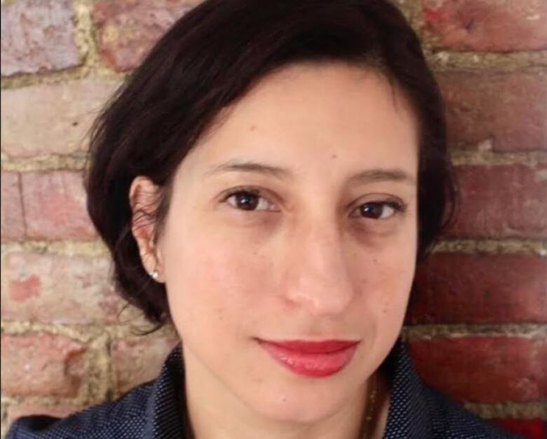 Closeup headshot of a young, dark-haired woman standing in front of a brick wall.