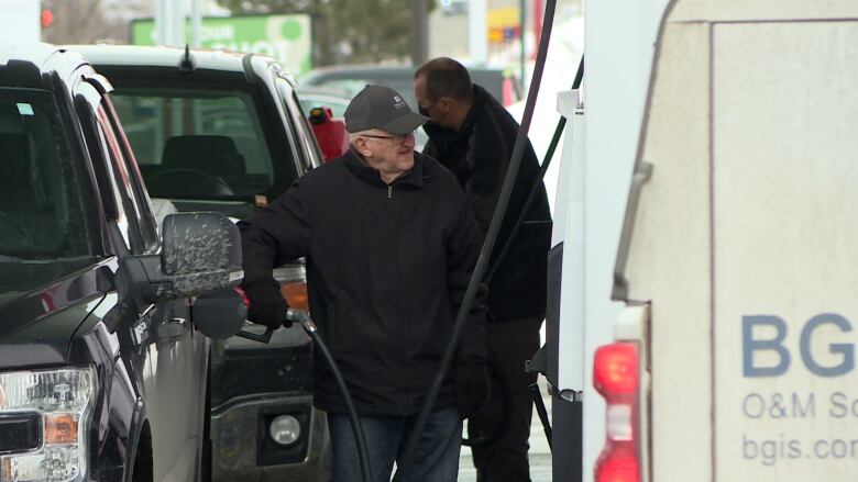 A man stands at a gas pump pumping fuel into his truck.