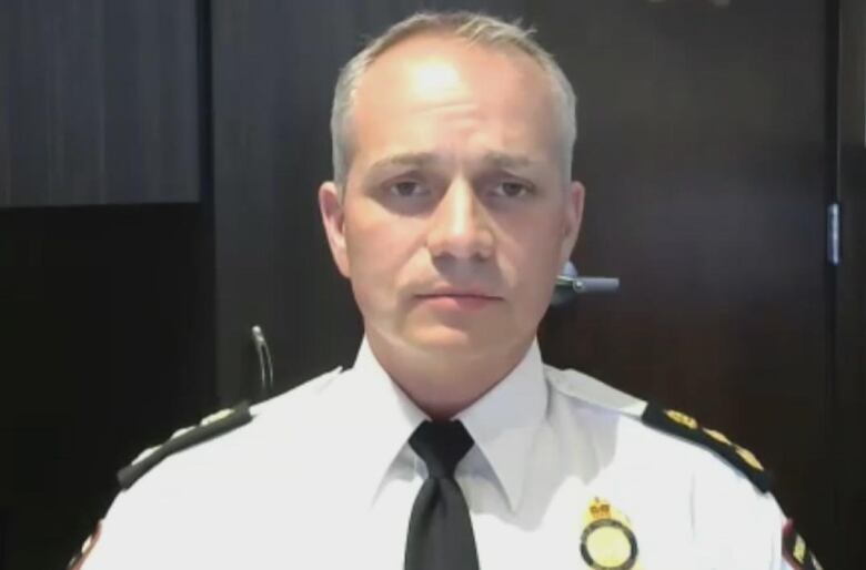 A man with grey hair in a police uniform looks at the camera.