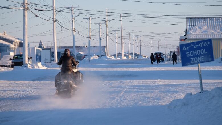 A snowmobiler drives down a snowy street.