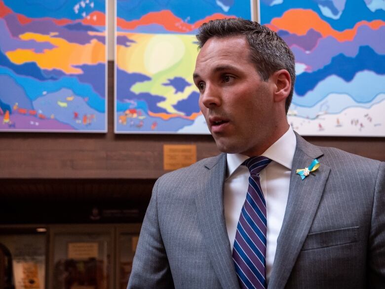 A man speaks to someone off-camera in front of bright paintings.