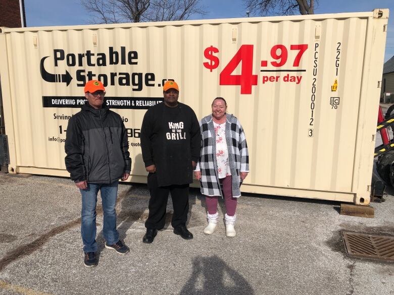 Three people stand beside a large yellow shipping container in a parking lot. 