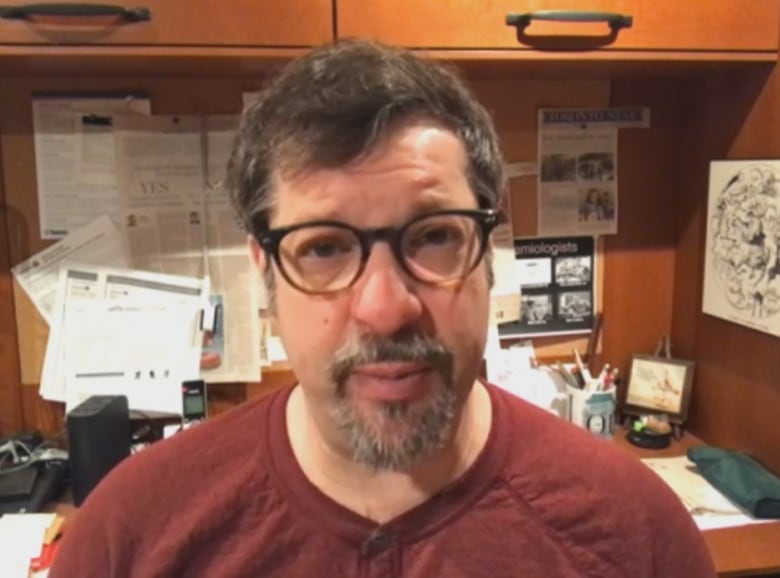 A portrait of a man sitting at a cluttered desk.