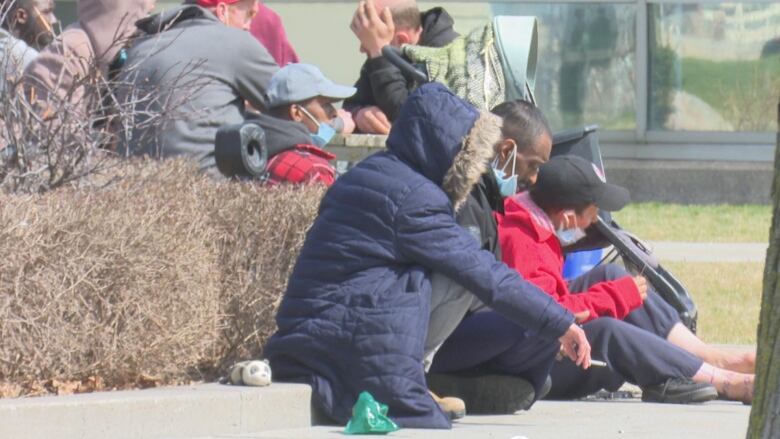 People experiencing homelessness sit outside of a temporary shelter in downtown Windsor.