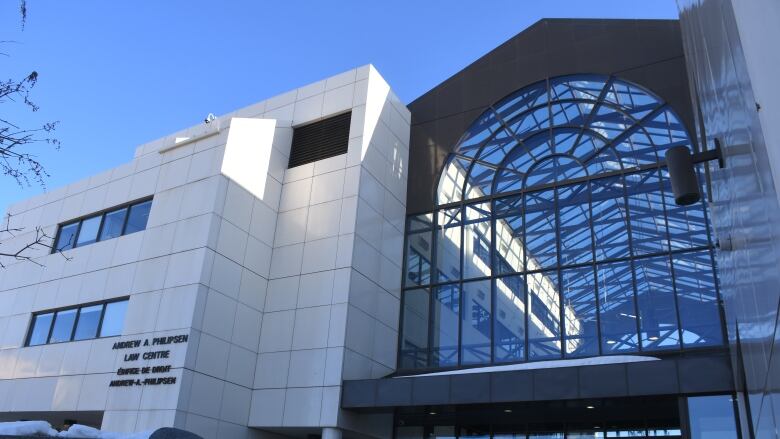 A multi-story building with a glass-door entryway and large windows above. To the left of the entry, the building is covered in large white tiles.