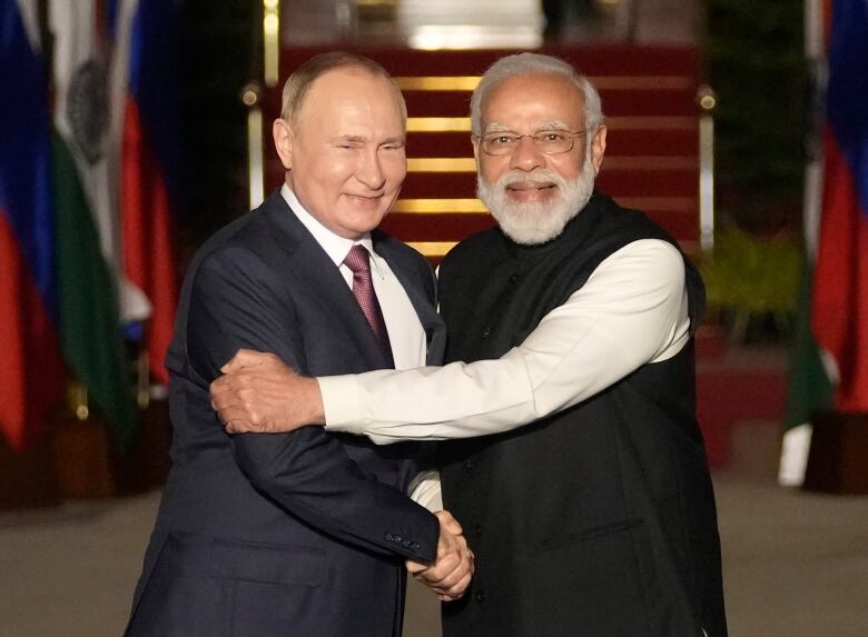 Two men pose for a photo as they shake hands. 