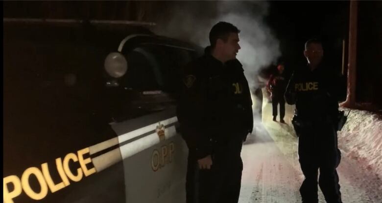 Police officers near a police vehicle. It's nighttime and winter.