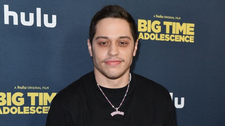 A man wearing a long sleeve black shirt faces the camera, with a slight smile on his face. 