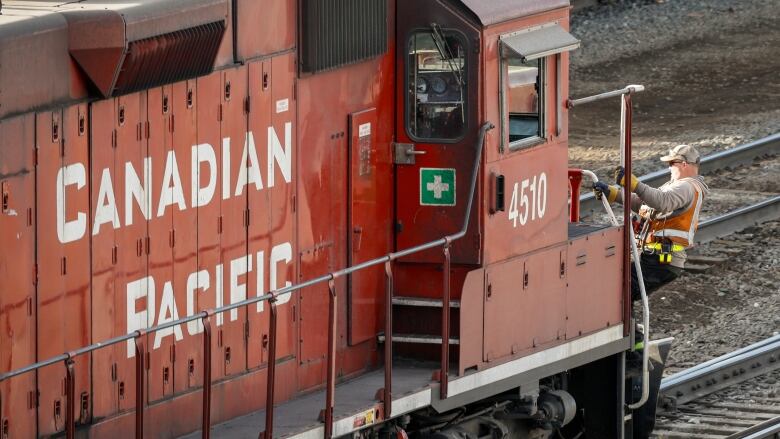 A railway worker boards the front of a red locomotive.