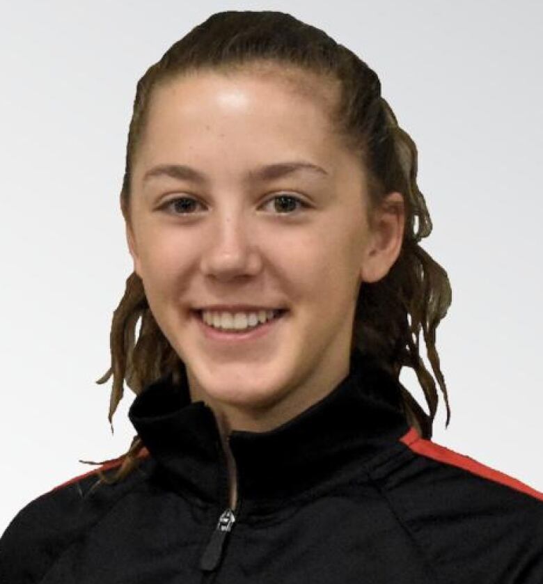 A young woman with brown hair in a dark tracksuit smiles at the camera.