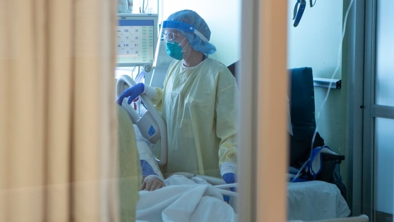 A nurse wearing full personal protective equipment tends to a COVID-19 patient behind a curtain in the intensive care unit.