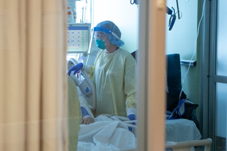 A nurse wearing full personal protective equipment tends to a COVID-19 patient behind a curtain in the intensive care unit.