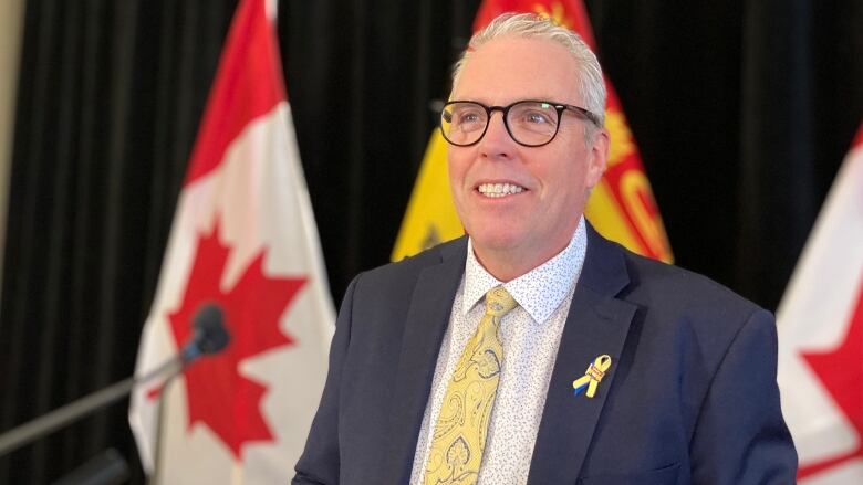 A man smiling in front of a New Brunswick flag with two Canadian flags on either side of it