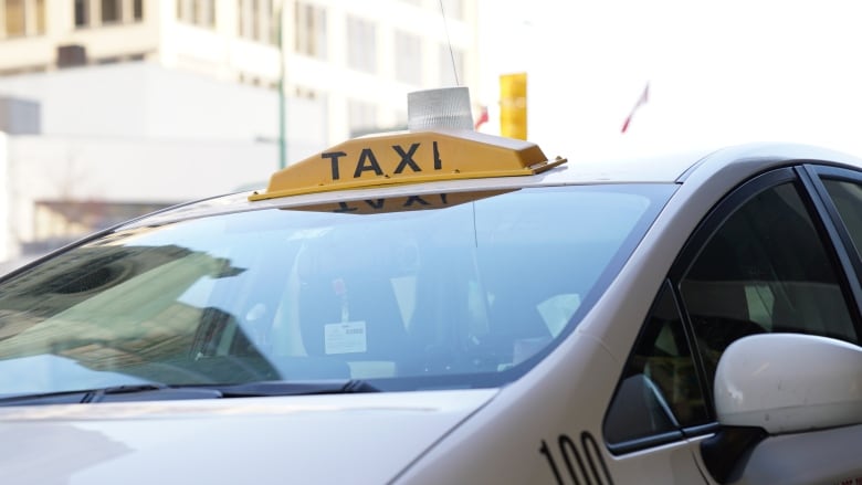 A yellow taxi sign is seen on top of a white car