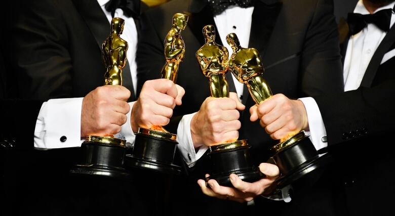 many hands holding oscar trophies