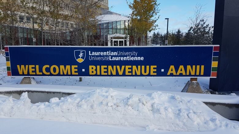 A blue banner with yellow lettering that says Laurentian University, Welcome, Bienvenue, Aanii with a snowbank in front of it.