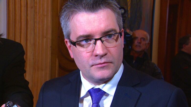 A close-up of a man with grey hair and glasses in a suit.