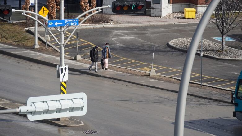 Two people walk on a sidewalk next to a city arterial road at the start of spring.