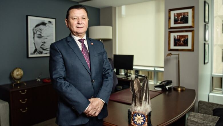 Canadian senator stands by his desk with his head dress sitting next to him. 