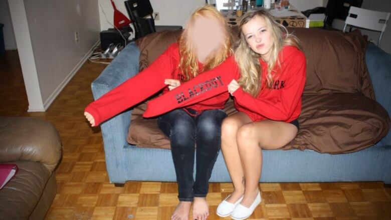 Two young women are shown in a university residence wearing identical red sweaters.