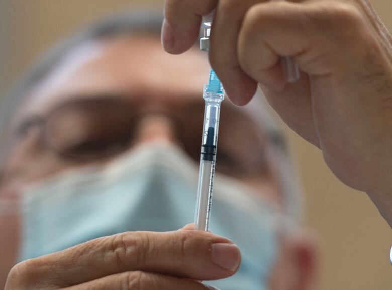 A man wearing a medical mask draws a vaccine dose from a vial.