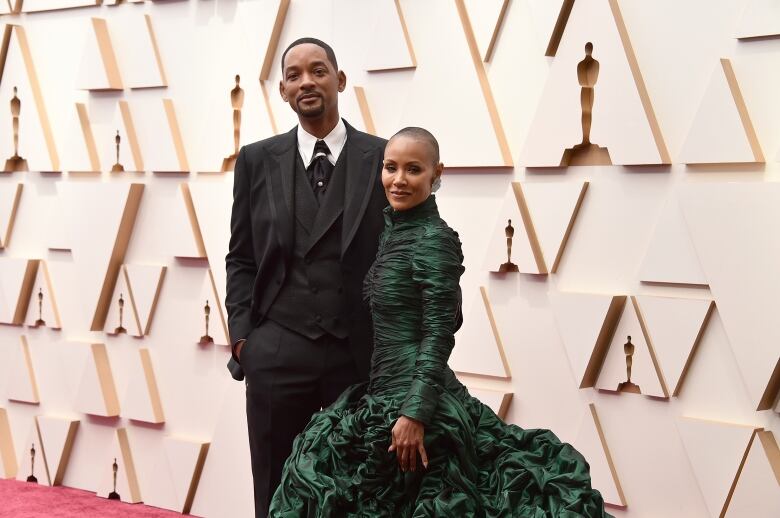 A couple dressed in formalwear attend a red carpet event.