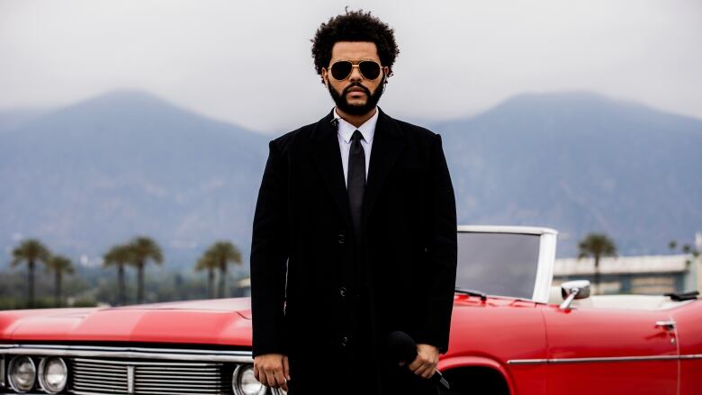 Man in suit stands in front of red car