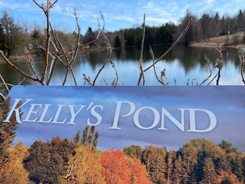 Sign saying Kelly's Pond in front of a pond. 