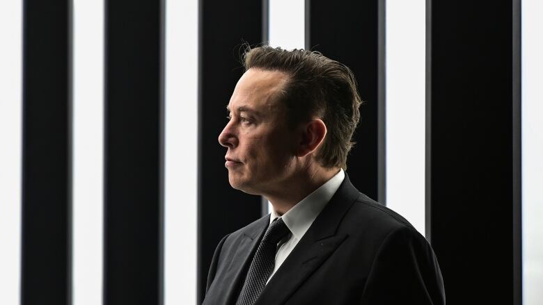 A profile shot of a man in a black suit and tie looking to the left of the frame.