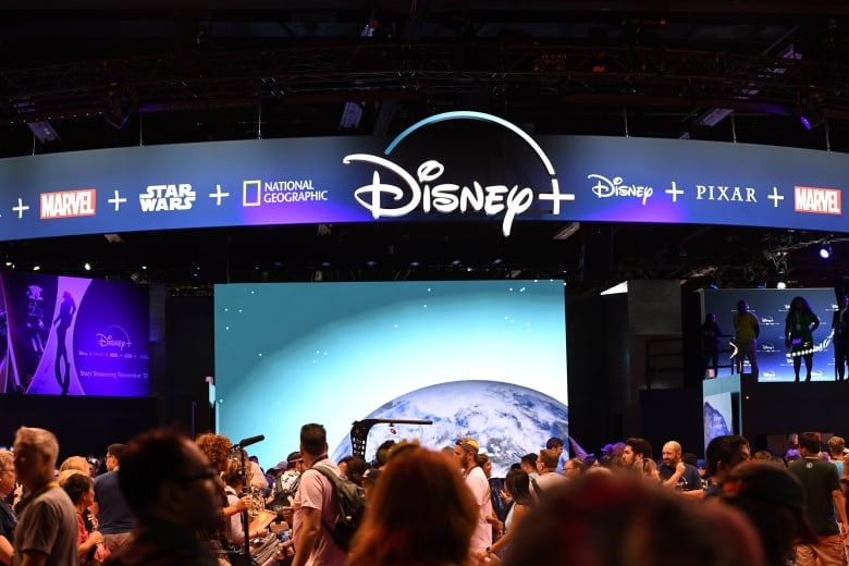 A crowd gathers under a Disney logo in a dark room.