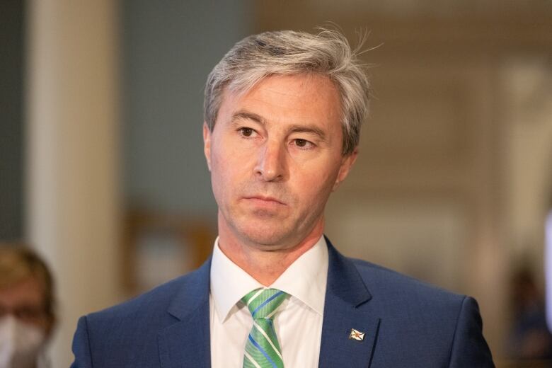 A grey-haired man in a suit and ties stares pensively.