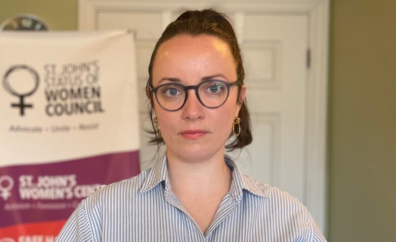 A woman with glasses looks at the camera. She's wearing a blue shirt.