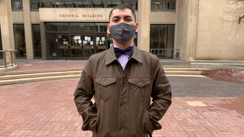 A man wearing a mask poses for a photo in front of Winnipeg city hall.