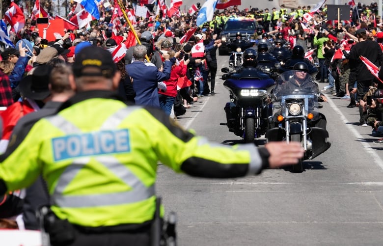 A police officer directs motorcycles as a big crowd looks on.