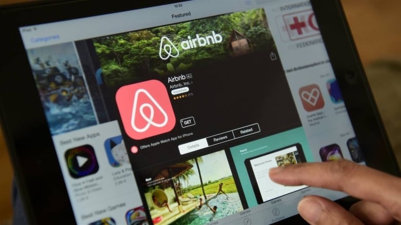 A finger points at the Airbnb app available for download on a tablet.