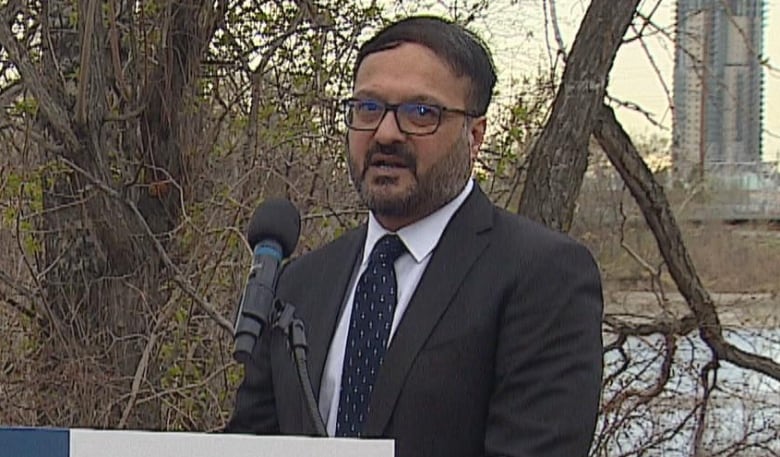 A man wearing a suit is pictured at a podium with a city skyline in the background.