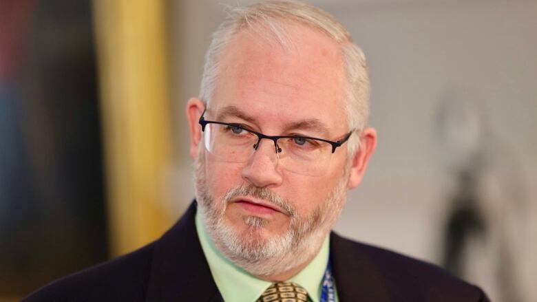 A man with white hair and a beard wears glasses.