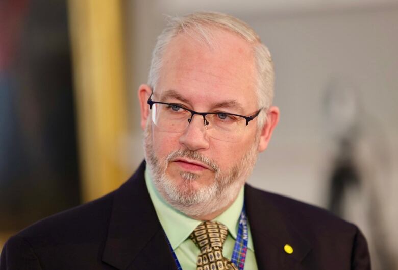 A man with white hair and a beard wears glasses.