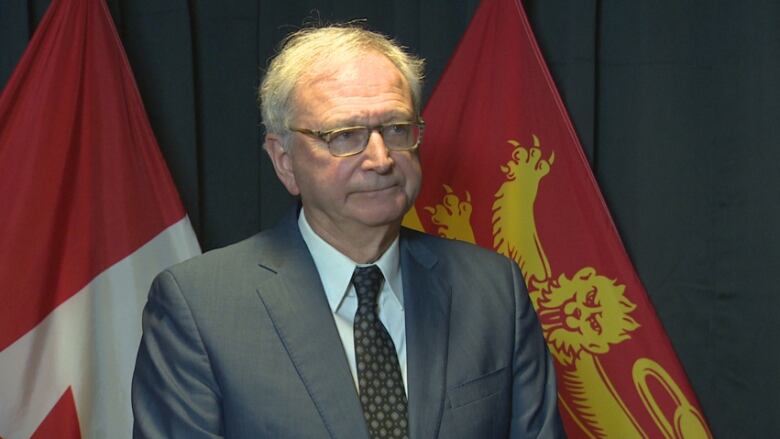 A man stands in front of the Canadian and New Brunswick flags.