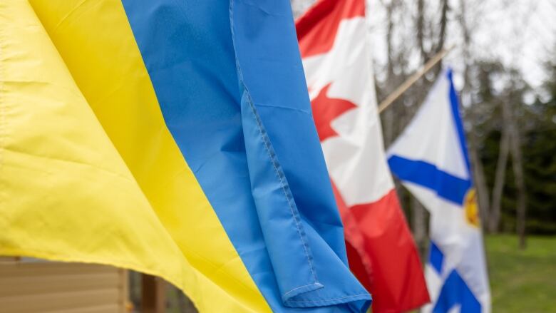 A Ukrainian flag, Canadian flag and Nova Scotian flag are seen side-by-side outside.