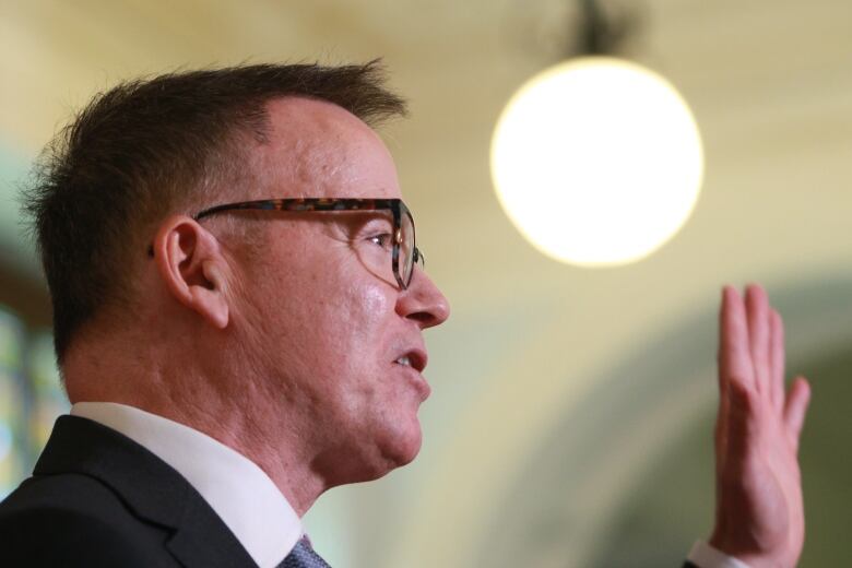 Kevin Falcon, a white man wearing glasses, gestures during a speech.