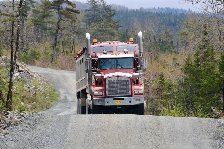 A semi truck drives on a  gravel road 