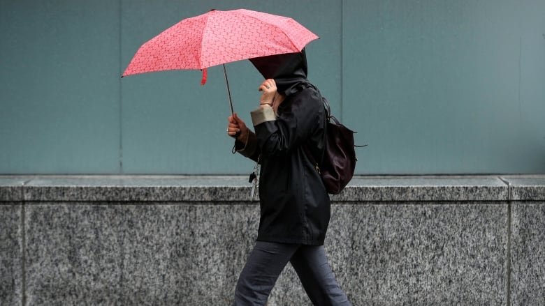 Someone in a dark coat and pants raises a red patterned umbrella.