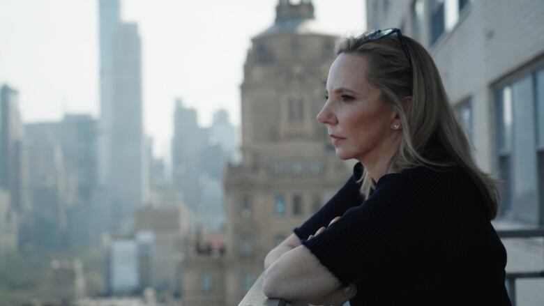 A woman stands on a balcony looking out at New York City.  