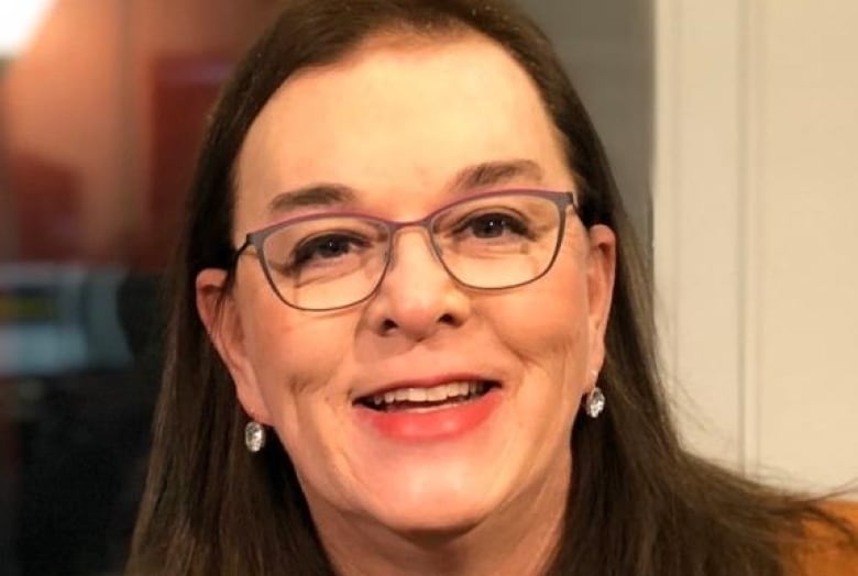 A smiling woman with glasses and an orange sweater.